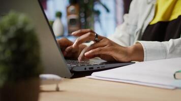 Teleworker typing on notebook keyboard in home office to write emails. Remote worker using laptop, composing documents in order to deliver finalized project paperwork, camera A close up shot video