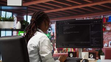 Programmer types code into PC, entering commands, running script. African american IT professional in apartment fixing errors in application, implementing new features, camera A video