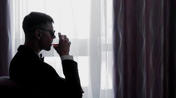 Man Drinking Wine in Silhouette by Window, Silhouetted man in formal attire drinks wine near a window, video