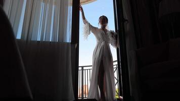 Bride in Sheer Robe Reaching Out, Elegant bride in a sheer robe with feathered sleeves stands at a doorway video