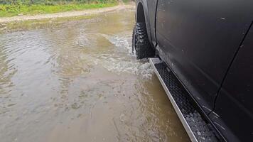 Truck Driving Through Shallow Water, Close-up view of a black truck navigating through shallow water, creating ripples and splashes on a rugged off-road terrain video