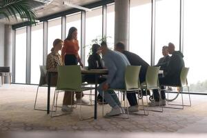 A diverse business team, working urgently around a conference table, collaborates on a meeting while their director, seated in a wheelchair, waits for their input photo