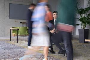 A businessman in a wheelchair navigating through a busy office, surrounded by his colleagues who are actively engaged in their work and collaboration photo