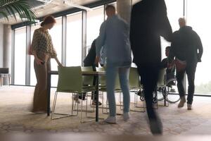 A diverse business team, working urgently around a conference table, collaborates on a meeting while their director, seated in a wheelchair, waits for their input photo