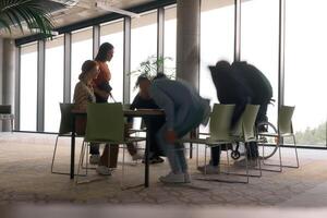 A diverse business team, working urgently around a conference table, collaborates on a meeting while their director, seated in a wheelchair, waits for their input photo