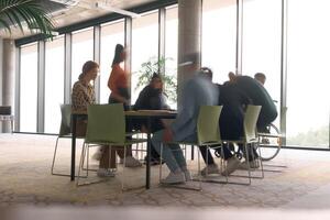 A diverse business team, working urgently around a conference table, collaborates on a meeting while their director, seated in a wheelchair, waits for their input photo