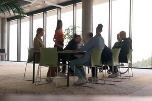 A diverse business team, working urgently around a conference table, collaborates on a meeting while their director, seated in a wheelchair, waits for their input photo