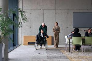 A diverse team of business colleagues, including a director in a wheelchair, engages in a collaborative discussion as they move together through a modern office space photo