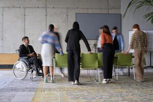 A diverse business team, working urgently around a conference table, collaborates on a meeting while their director, seated in a wheelchair, waits for their input photo