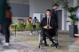 A businessman in a wheelchair navigating through a busy office, surrounded by his colleagues who are actively engaged in their work and collaboration photo