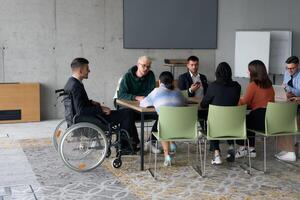 A diverse group of business professionals, including a man in a wheelchair, collaborate during a meeting in a modern office environment. photo