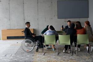 A diverse group of business professionals, including a man in a wheelchair, collaborate during a meeting in a modern office environment. photo