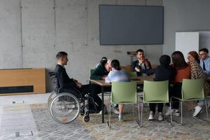 A diverse group of business professionals, including a man in a wheelchair, collaborate during a meeting in a modern office environment. photo