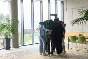A diverse group of professionals standing in a supportive circle, embracing each other in a modern office space filled with natural light. photo