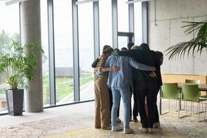 A diverse group of professionals standing in a supportive circle, embracing each other in a modern office space filled with natural light. photo