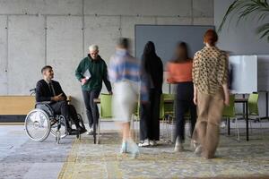 A diverse business team, working urgently around a conference table, collaborates on a meeting while their director, seated in a wheelchair, waits for their input photo
