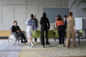 A diverse business team, working urgently around a conference table, collaborates on a meeting while their director, seated in a wheelchair, waits for their input photo