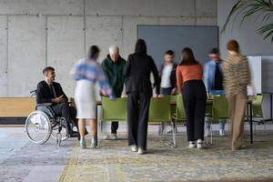 A diverse business team, working urgently around a conference table, collaborates on a meeting while their director, seated in a wheelchair, waits for their input photo