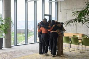 A diverse group of professionals standing in a supportive circle, embracing each other in a modern office space filled with natural light. photo