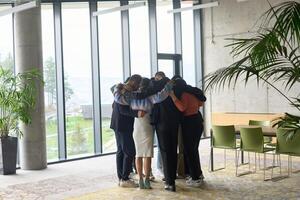 A diverse group of professionals standing in a supportive circle, embracing each other in a modern office space filled with natural light. photo