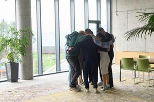 A diverse group of professionals standing in a supportive circle, embracing each other in a modern office space filled with natural light. photo