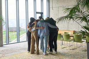 A diverse group of professionals standing in a supportive circle, embracing each other in a modern office space filled with natural light. photo