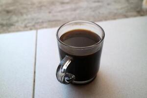 a glass of black coffee in a glass cup photographed from the side, during the day photo