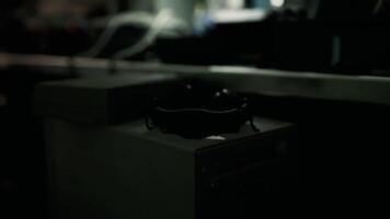 A black, circular object is placed on a plain table amid a low lit environment video