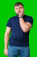 Young man with a contemplative expression leaning against green backdrop while resting his head on his hand photo