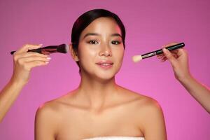 Two artists applying makeup on a model with pink background during a beauty session in a studio setting photo