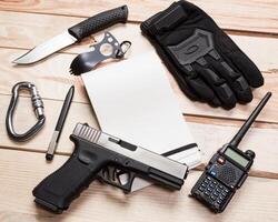 Assault rifle, gun, knife with sheath, compass and notebook with pen on table. photo
