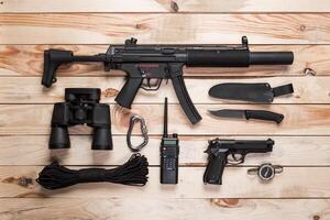 Assault rifle, gun, knife with sheath, compass and notebook with pen on table. photo