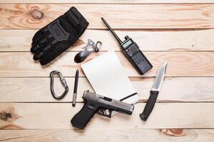 Assault rifle, gun, knife with sheath, compass and notebook with pen on table. photo