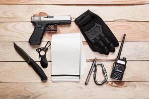Assault rifle, gun, knife with sheath, compass and notebook with pen on table. photo