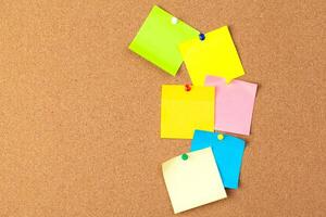 Cork board with several colorful blank notes with pins photo
