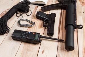 Assault rifle, gun, knife with sheath, compass and notebook with pen on table. photo