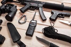 Assault rifle, gun, knife with sheath, compass and notebook with pen on table. photo