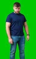 A man stands confidently on a bright green background wearing a dark t-shirt and jeans photo