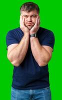 Young man with a contemplative expression leaning against green backdrop while resting his head on his hand photo
