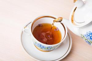 Old-style porcelain kettle pouring tea from jug to cup of tea photo