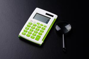 Calculator with a magnifying glass on a black background photo