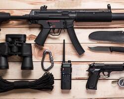 Assault rifle, gun, knife with sheath, compass and notebook with pen on table. photo