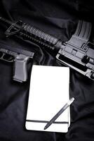 Rifle, gun, knife with sheath, compass and notebook with pen on on black cloth photo