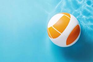 A bright orange and white volleyball floating on a tranquil blue pool's surface during a sunny afternoon photo