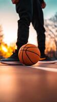 A person standing over a basketball during sunset on an outdoor court, capturing the lively ambiance of an evening game photo