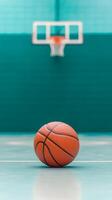 A basketball sits on the court before a green backdrop, focusing on the ball with the hoop visible in the background during a practice session photo