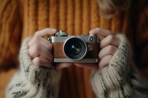 A person in a warm sweater holds a vintage camera, capturing memories in a cozy setting photo
