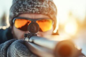 Hunter aiming a rifle in a snowy landscape during sunset with protective eyewear and winter attire photo