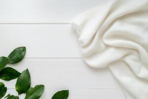 Soft white blanket draped over wooden surface with green leaves arranged alongside for a cozy, natural look photo