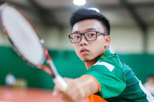 Young athlete in green shirt prepares to serve in a badminton match at an indoor court during a local tournament photo